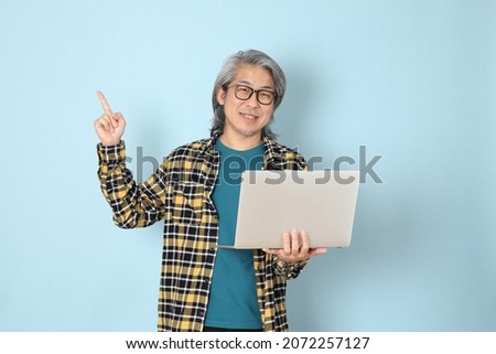 The senior Asian man with yellow plaid shirt standing on the blue background.