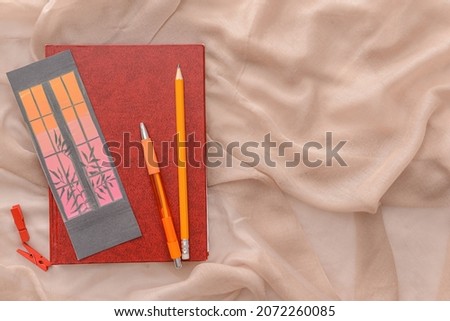 Book with bookmark, pencil and pen on color background