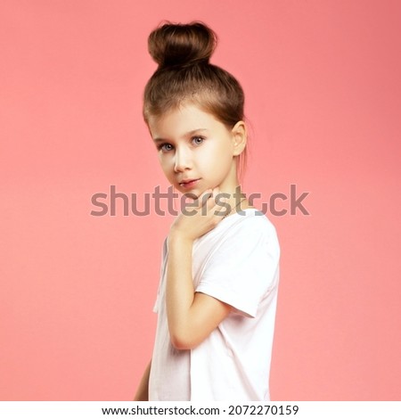 Fashionable studio portrait of cute little pretty caucasian girl posing in t-shirt fashionable style on pink background