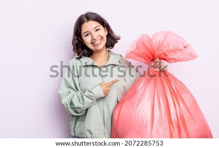 pretty young woman smiling cheerfully, feeling happy and pointing to the side. trash bag concept