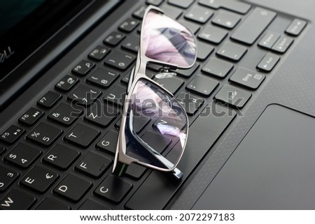 Clear reading glasses, black rim, on a laptop keypad, no people.
