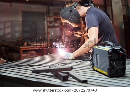welder in a helmet works as a welding machine in a workshop.sparks from welding Royalty-Free Stock Photo #2072298743