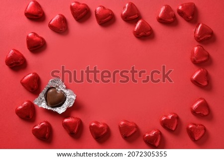 Romantic chocolate sweets as heart in red foil as frame on red background with copy space. Valentine's day greeting card. Love concept.