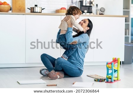 Shot of young beautiful mother playing and having fun on the floor with her son in living room at home.