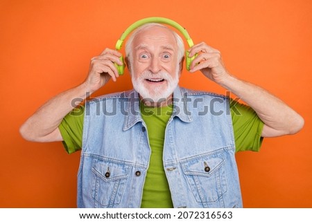 Photo of pretty impressed retired man wear vintage jeans waistcoat listening music headphones isolated orange color background