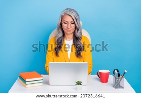 Photo of confident shiny mature woman wear yellow jacket spectacles working modern device workshop isolated blue color background