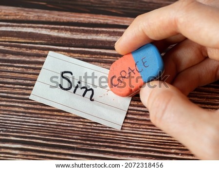 A handwritten word sin with a hand holding a rubber eraser with grace text on wooden background. Christian biblical concept of grace, mercy, sacrifice, and sacrifice of God Jesus Christ. A close-up. Royalty-Free Stock Photo #2072318456