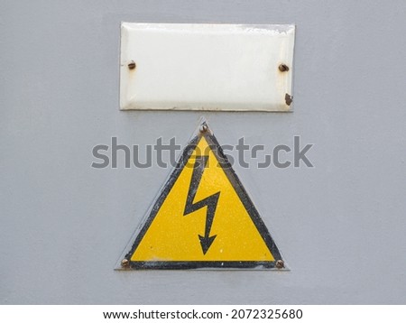 Yellow sign warns of high voltage on an old gray metal door close-up