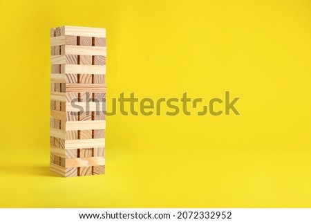 Jenga tower made of wooden blocks on yellow background, space for text Royalty-Free Stock Photo #2072332952