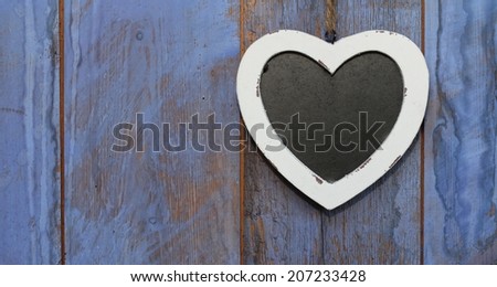 Heart shaped shabby chic chalk board with white wooden frame hanging on rough wooden painted blue, purple barn door