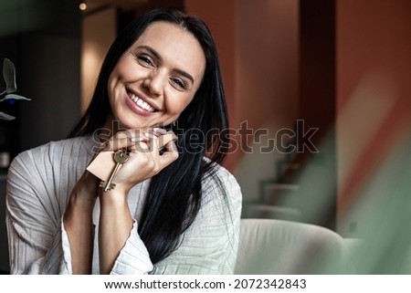 Laughing young brunette woman holding keys from new flat or house enjoying independence with positive emotion. Smiling female with natural beauty owner of apartment celebrating buying purchasing