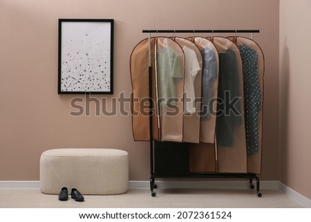 Garment bags with clothes hanging on rack in room Royalty-Free Stock Photo #2072361524