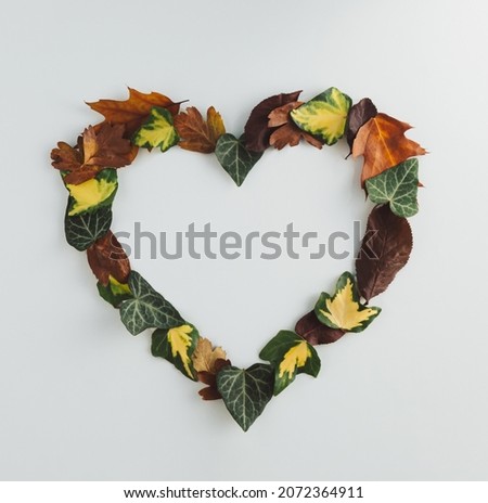 Creative heart shape made of colorful autumn or fall leaves. Flat lay, top view. Changing season concept. Nature composition with paper card note copy space.