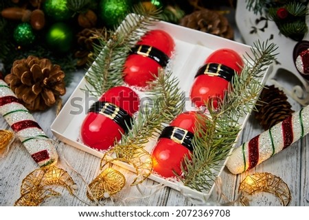 Red Christmas dessert in the form of mousse on the background of candles, garlands, fir branches and cones