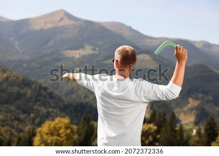Man throwing boomerang in mountains on sunny day, back view Royalty-Free Stock Photo #2072372336