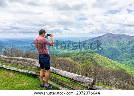 Devil's Knob overlook with man standing photographing taking picture of mountain view by wooden rustic countryside fence at Wintergreen resort town by Virginia Blue Ridge mountains