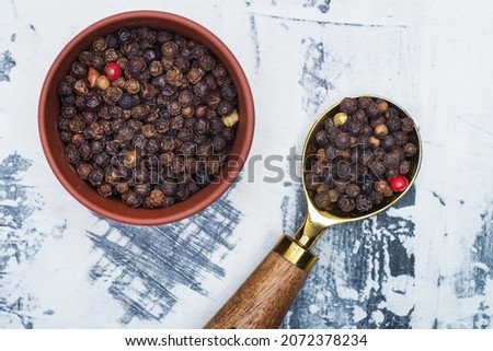 black pepper in a spoon and a clay bowl on a gray background. view from above