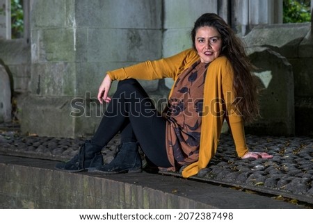 Argentinian woman with long wavy brown hair, sitting on the floor and yellow clothes