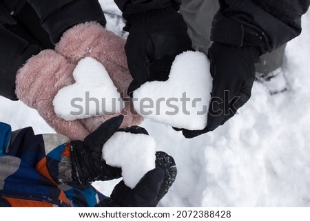 Love Winter. Hands of adults and a child in winter clothes, holding 3 hearts made of snow. Rest in the winter season, an active lifestyle. Friendly family. Snow games