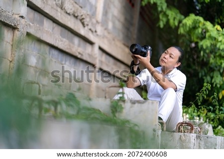 Professional Asian Chinese - Thai Camera man posture and focus in viewfinder and LED screen on mirrorless camera medium format in construction concrete area.