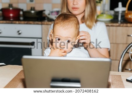 Motherhood, parenting, childcare. Mom and child using tablet, watching educational children's video. Baby boy sucking fingers and looking at display of gadget while sitting with mother, indoors.