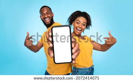 Use this new mobile app. Joyful African American couple pointing at smartphone with empty white screen, advertising your website, mockup. Selective focus. Banner design