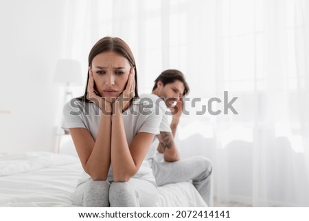 Disappointed young caucasian lady sits on bed, ignores offended man. Frustrated sad wife sit on bed thinking about relationship problems, thoughtful couple after quarrel, upset lovers consider parting Royalty-Free Stock Photo #2072414141