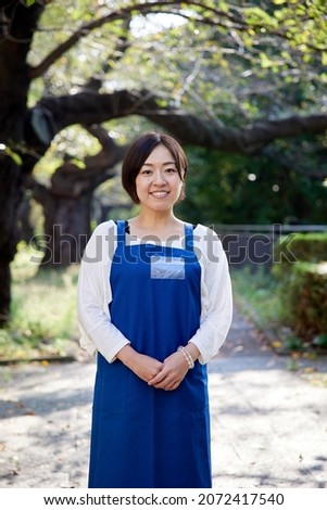 Asian woman wearing a blue apron and smiling in the fresh green