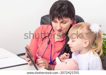 Doctor pediatrician shows cartoons on the tablet of a little girl 3-4 years old. The concept of psychological contact with a child at a doctor, healthcare