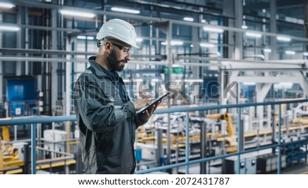 Car Factory Engineer in Work Uniform Using Tablet Computer. Automotive Industry 4.0 Manufacturing Facility Working on Vehicle Production with Robotic Arms Technology. Automated Assembly Plant. Royalty-Free Stock Photo #2072431787