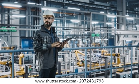 Car Factory Engineer in Work Uniform Using Tablet Computer. Automotive Industry 4.0 Manufacturing Facility Working on Vehicle Production with Robotic Arms Technology. Automated Assembly Plant. Royalty-Free Stock Photo #2072431793
