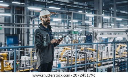 Car Factory Engineer in Work Uniform Using Tablet Computer. Automotive Industry 4.0 Manufacturing Facility Working on Vehicle Production with Robotic Arms Technology. Automated Assembly Plant. Royalty-Free Stock Photo #2072431796