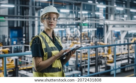 Female Car Factory Engineer in High Visibility Vest Using Laptop Computer. Automotive Industrial Manufacturing Facility Working on Vehicle Production with Robotic Arms. Automated Assembly Plant. Royalty-Free Stock Photo #2072431808
