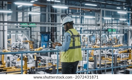 African American Car Factory Engineer in High Visibility Vest Using Tablet Computer. Automotive Industrial Manufacturing Facility Working on Vehicle Production on Automated Technology Assembly Plant. Royalty-Free Stock Photo #2072431871