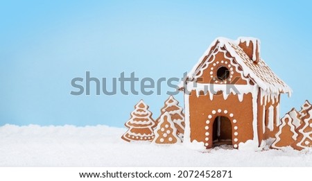 Christmas greeting card with gingerbread house, gingerbread fir trees in snow and copy space