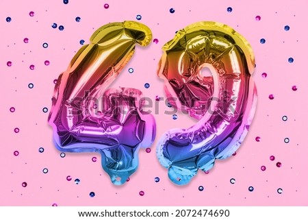 Rainbow foil balloon number, digit forty nine on a pink background with sequins. Birthday greeting card with inscription 49. Top view. Numerical digit. Celebration event, template.