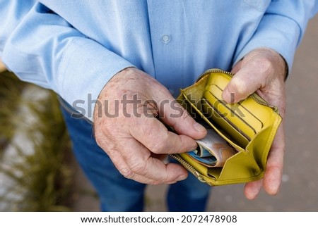 Senior man looks in his purse with Euro banknotes. Old man puts euro bills in his wallet. A wallet with the last money in the hands of an elderly man. A pensioner counts out the rest of his pension Royalty-Free Stock Photo #2072478908