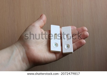 A woman is hand holding a negative and positive pregnancy test on a light background. Motherhood, pregnancy, the concept of birth control. Health problems and problems with conception. Copy space.