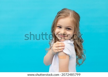 a little girl child with a patch on her arm after vaccination in a white T-shirt on a blue background in the studio, space for text, the concept of vaccination, health and medicine Royalty-Free Stock Photo #2072485799