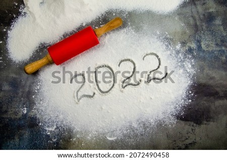 2022 sign is painted on flour. inscription 2022 is made of flour on black concrete background. Top view, flat lay, space for text. rolling pin, flour and numbers 2022. Christmas culinary background