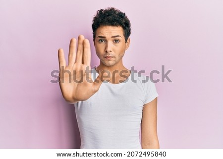 Young handsome man wearing casual white t shirt doing stop sing with palm of the hand. warning expression with negative and serious gesture on the face. 