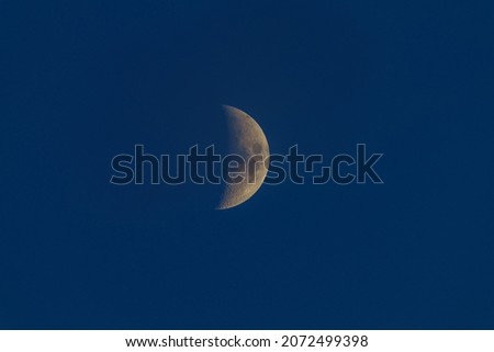 partly illuminated Moon with visible craters by the sun from 40 percent in a blue sky without clouds