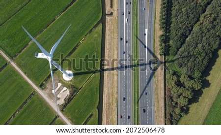 Aerial top down view of wind turbine and highway with traffic moving both ways turbines creating electricity in eco-friendly way for sustainable renewable powering vehicles Royalty-Free Stock Photo #2072506478