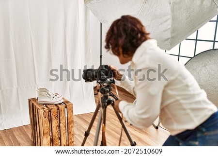 Young hispanic photographer woman on back view using camera at photo studio.