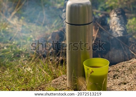 a steel thermos flask next to the mug. a hot drink from a thermos. breakfast in nature. background picture.