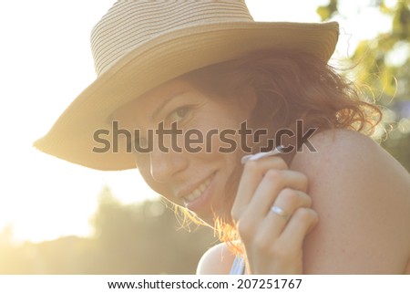 Beautiful girl with a hat smelling a flower, enjoying sunny summer day