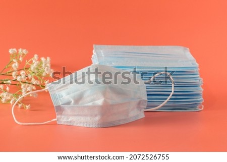 There are a lot of new medical facial three-layer masks stacked high and one mask lies next to it on a pink background
