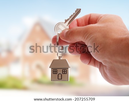 Holding house keys on house shaped keychain in front of a new home Royalty-Free Stock Photo #207255709