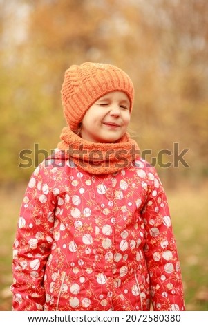 Portrait of a beautiful girl in an orange hat and a scarf, the child smiles, a walk in the autumn park.
