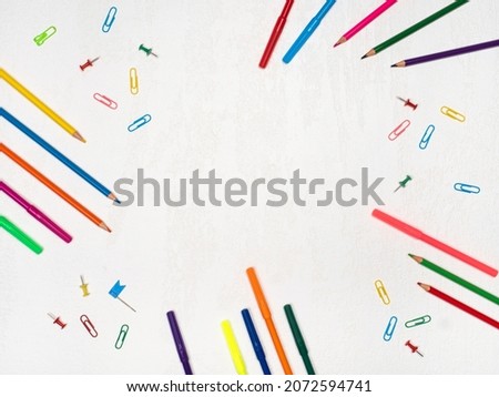 Colored stationery frame: pencils, markers, paper clips on white background with place for text. Flatlay pattern with colorful objects for drawing and writing at school, office with copy space. 